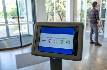 A digital feedback kiosk with a touchscreen interface displays a satisfaction survey with...