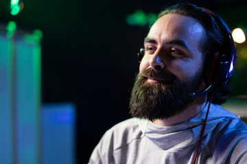 Smiling man relaxing by playing science fiction FPS videogame with friends on PC at computer desk at night. Close up of upbeat gamer communicating with teammates, shooting enemies in online shooter