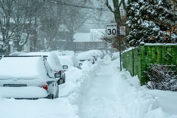 time to dig out: snow covered cars parked on snow choked residential street with cleared sidewalk...
