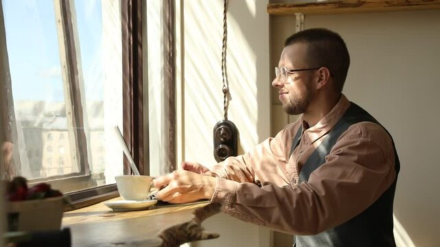 It man with glasses by the window working at a computer on a sunny day