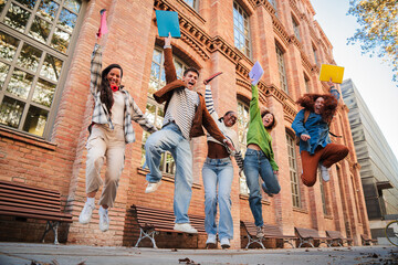 Excited Students Jumping Joyfully Together Celebrating Their Achievements While Holding Colorful...