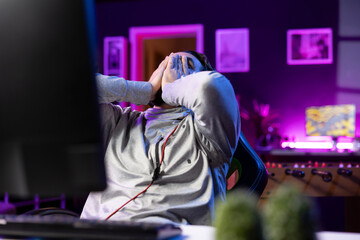 Player upset after losing while playing videogame, putting face in hands in frustration. Gamer at...