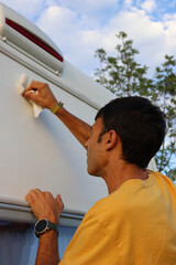 Camper cleaning motorhome exterior on a sunny day.