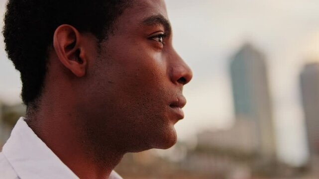 Young man looks thoughtfully at the city skyline during sunset. He appears contemplative and hopeful about the future.