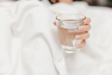 Woman holding glass of water in hand, laying in bed with white comforter