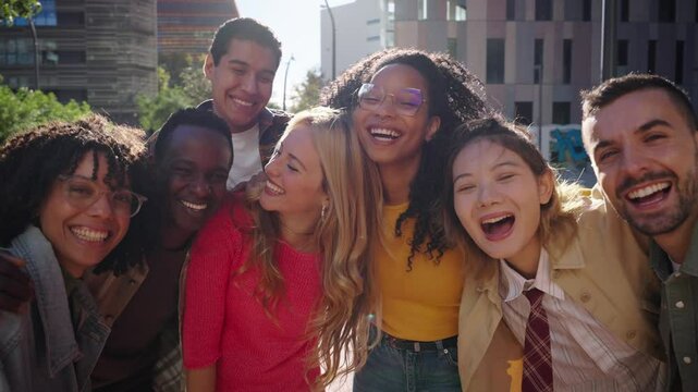Laughing group of young diverse friends looking joyful at camera having fun together outdoors. Generation z of multiracial cheerful people posing smiling standing embracing in community at city street