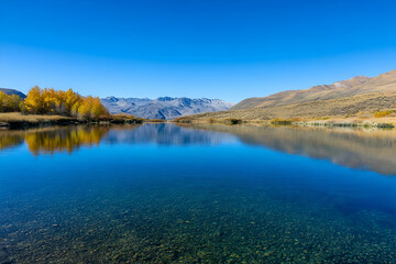 Crystal-clear lake reflecting bright autumn foliage under a cloudless blue sky