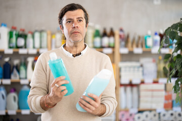 Among shop windows, man buyer leisurely examines goods and chooses shampoo or shower gel. Client...