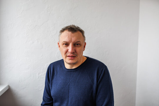 Portrait of a cheerful middle-aged man wearing a gray hoodie, standing against a textured stone wall in natural light. - Powered by Adobe