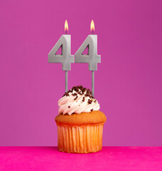 Birthday candle number 44 with cupcake on violet background.