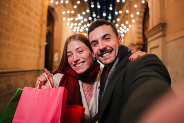 Happy couple enjoying their buying experience with shopping bags while taking a selfie together, capturing a joyful moment filled with excitement and love during a festive evening outing in the city