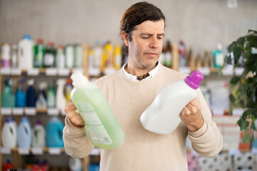Adult man buyer chooses laundry detergent in household chemicals store