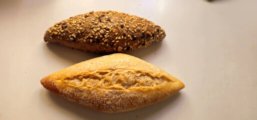 Two types of bread on a white surface; one is light with a crisp crust and a deep slash, the other is darker, covered with mixed seeds and has a rough texture;