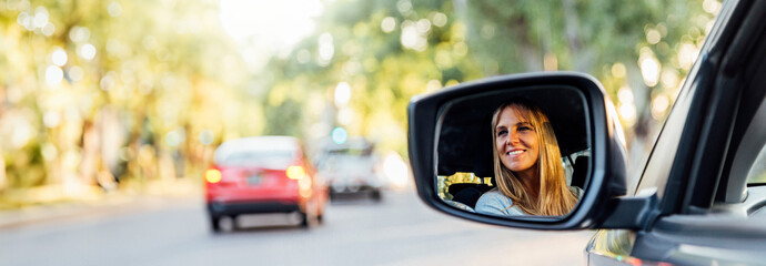 Happy beautiful middle-aged woman in the rearview mirror of her new car. Horizontal photo in banner...