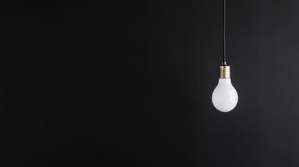 Single lightbulb hanging against black wall, idea concept