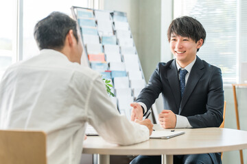 男性客と商談・接客・打ち合わせする若いアジア人ビジネスマン（自動車・保険） 