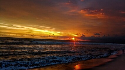 Obraz premium The image captures a breathtaking sunset over the ocean. The sun is partially set on the horizon, casting a golden glow across the sky and reflecting on the water