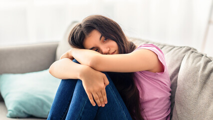Unhappy teen girl feeling depressed or desperate, sitting on couch at home. Indian asdolescent...
