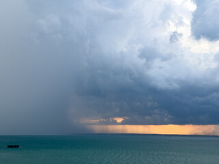 Obraz premium Rain Cloud covering gorgeous golden sunset over weahter change in tropical blue green sea in Darwin Australia - concept of nature, storm, natural