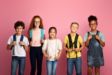Back to school again. Joyful children with backpacks standing together on pink background