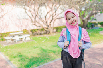 Happy Muslim student in pink hijab with blue backpack standing in spring garden. Natural lighting, outdoor campus lifestyle. Education concept.
