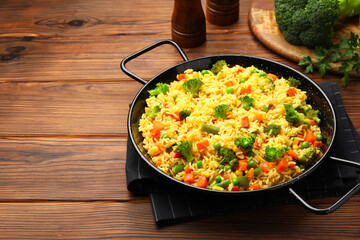 Tasty rice with vegetables in baking dish on wooden table, space for text