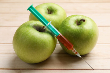 GMO concept. Fresh apples and syringe on wooden table, closeup