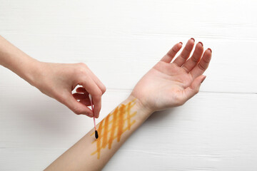 Obraz premium Woman applying topical iodine with cotton swab on hand at white wooden table, top view