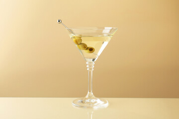 Martini cocktail with olives in glass on beige table