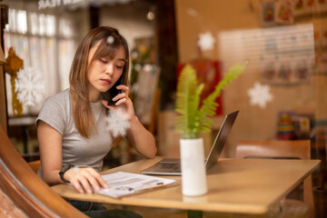 A woman is talking on her cell phone while sitting at a table with a laptop