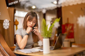 A woman is talking on her cell phone while sitting at a table with a laptop