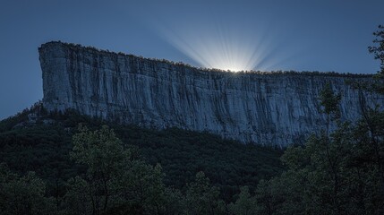 Majestic cliff at sunset with rays of light emerging behind, surrounded by lush forest