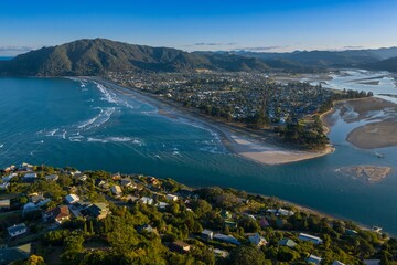 Obraz premium Coastal Pauanui nestled beside a bay, with homes lining the shore and a sandy beach. Aerial view of a tranquil seaside community. Tairua, Coromandel Peninsula, New Zealand