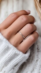 A models hand is displaying a sleek silver ring highlighted by gentle lighting on a marble surface
