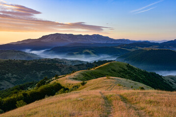 Fototapeta premium Mountain landscape with grassy hills forest and morning fog Sunrise sky adding color to the scene