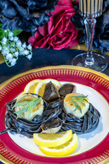Scallops on a bed of black squid ink pasta with black garlic on a red plate