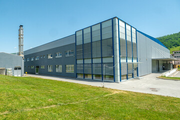 Large industrial building with gray and blue exterior under a bright blue sky surrounded by green grass