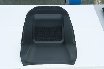 Molded black car part with a mesh pocket laying on a white surface studio lighting for transport and storage