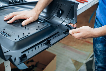 A person works with their hands assembling an intricate black plastic component in an industrial...
