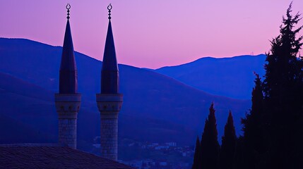 Twin minarets silhouetted against a vibrant purple sunset over distant mountains and trees