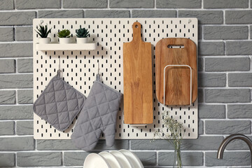White pegboard with cutting boards, mitts and houseplants hanging on grey brick wall in kitchen