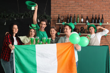 Group of young people with beer and Irish flag celebrating St. Patrick's Day in pub