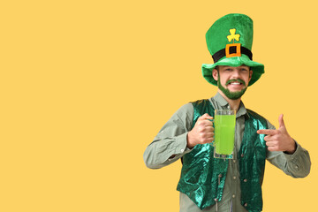 Young man in leprechaun hat with green beard pointing at glass of beer on yellow background. St....