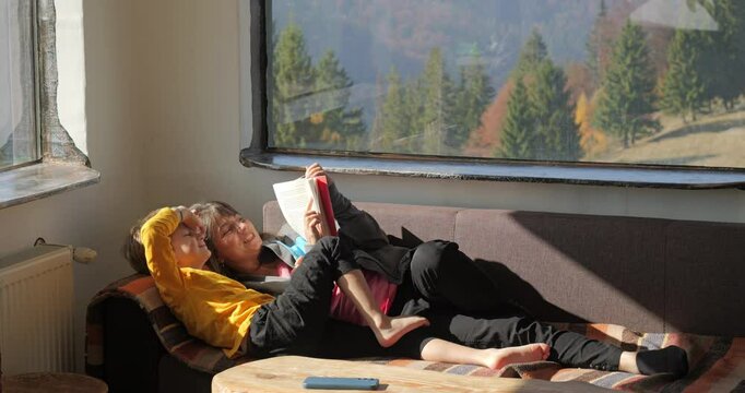 Mother and son lying on sofa and have fun by reading a book in a mountain rustic chalet