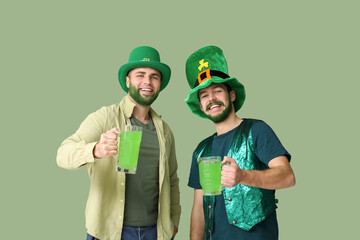 Happy young men in leprechaun hats with green beards holding glasses of beer on green background....