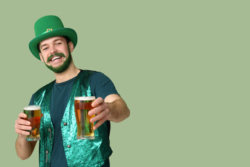 Young man in leprechaun hat with green beard holding glasses of beer on green background. St....
