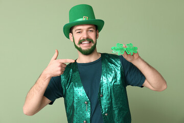 Young man in leprechaun hat with green beard pointing at decorative glasses in shape of clover on...