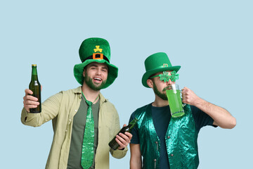 Young men in leprechaun hats with green beards holding bottles and glass of beer on blue...
