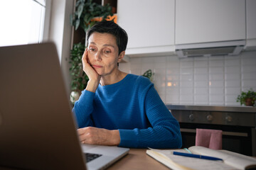 Indifferent mature woman exhausted from working on laptop and taking notes even at home, burnout....