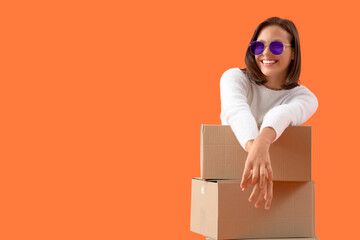 Beautiful young happy woman in new sunglasses with many parcels on orange background